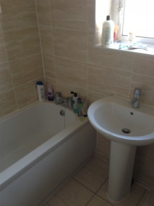 Sink fitted to cream tile beneath the window next to the bath