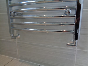 Chrome Towel Radiator with water pipes coming out of the wall