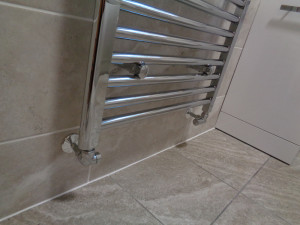 Chrome heating pipes coming from wall into the wall mounted towel warmer